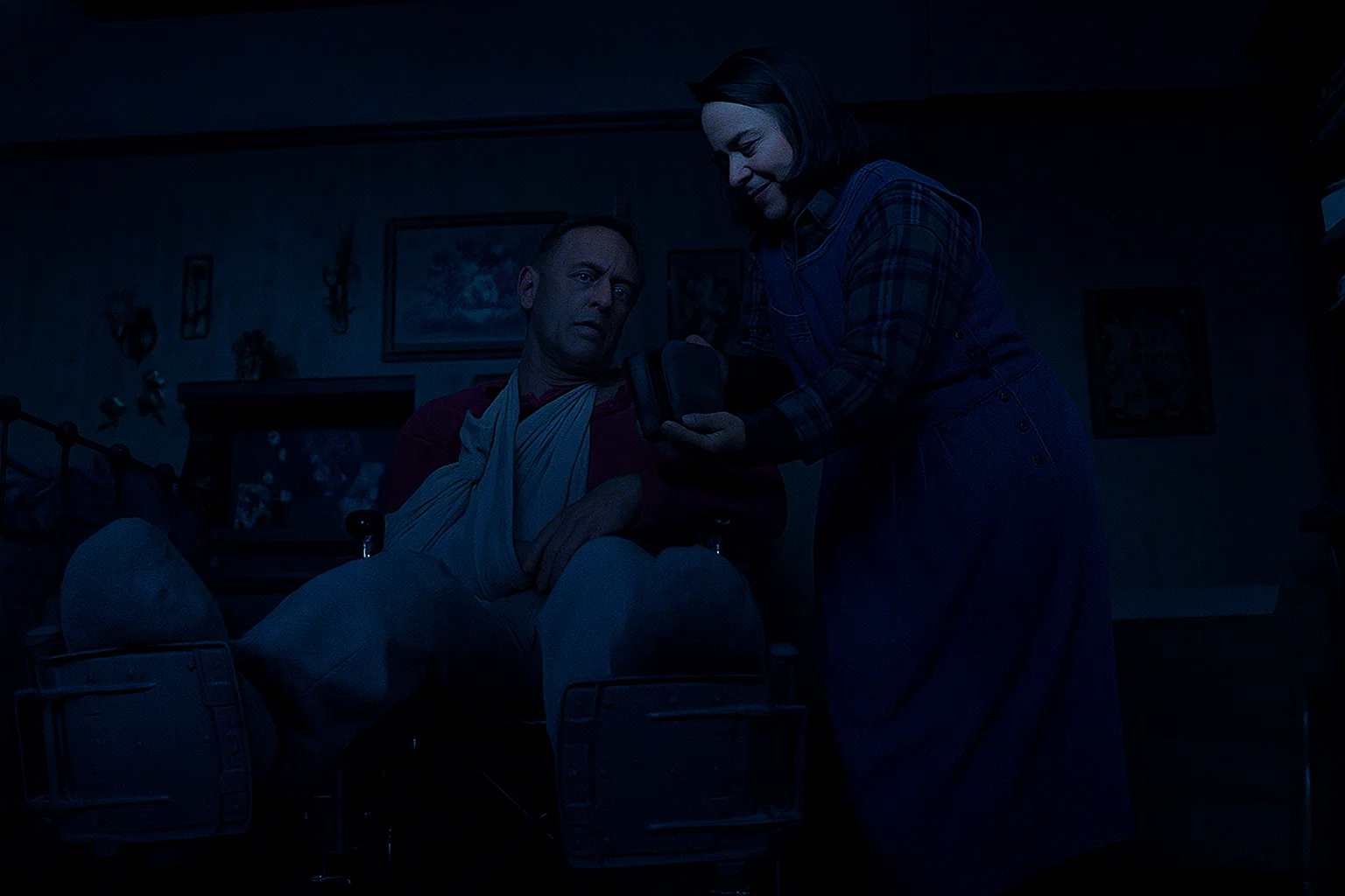 Annie Wilkes holding a sledgehammer beside Paul Sheldon’s bed in Misery, depicting the real-life inspired psychological thriller by Stephen King.
